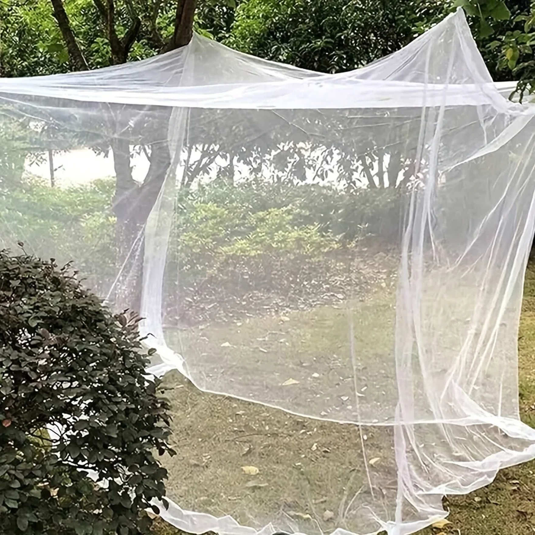 Moustiquaire cube de camping blanche suspendue au-dessus d'un couchage en extérieur - Moustigo